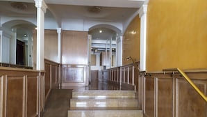 A grand staircase with marble steps and wooden paneling, leading to a high-ceilinged area with arched doorways.