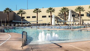 A swimming pool with a water fountain, palm trees, and a building with a beige facade in the background. - Private oasis to relax in the sun. (Sun City West)