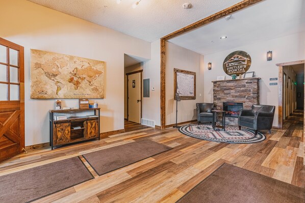 A lobby with a wooden floor, a world map on the wall, a stone fireplace, leather chairs, and a reception desk.