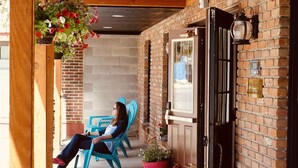 A brick building with a wooden ceiling and a door. There are two blue chairs and two red chairs outside.