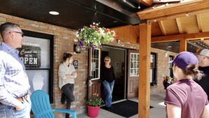A brick building with a sign indicating it's open, a hanging flower basket, and a blue chair outside.