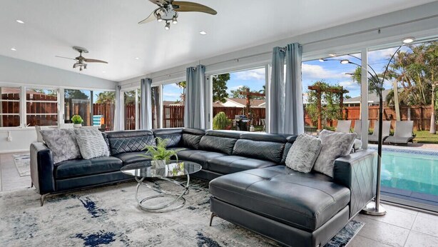 A spacious living room with a large sectional sofa, a glass coffee table, and a ceiling fan. - 3/2 Heated Pool House Walking Distance to Beach (Naples)