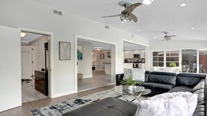 A modern living room with a black leather sofa, a glass coffee table, and a ceiling fan. - 3/2 Heated Pool House Walking Distance to Beach (Naples)