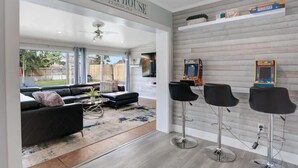 A modern living room with a black sofa, a coffee table, and a rug. There are three black bar stools against a wall with framed pictures. - 3/2 Heated Pool House Walking Distance to Beach (Naples)