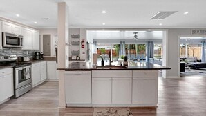 A modern kitchen with white cabinetry, a central island, and a view to a living area. - 3/2 Heated Pool House Walking Distance to Beach (Naples)