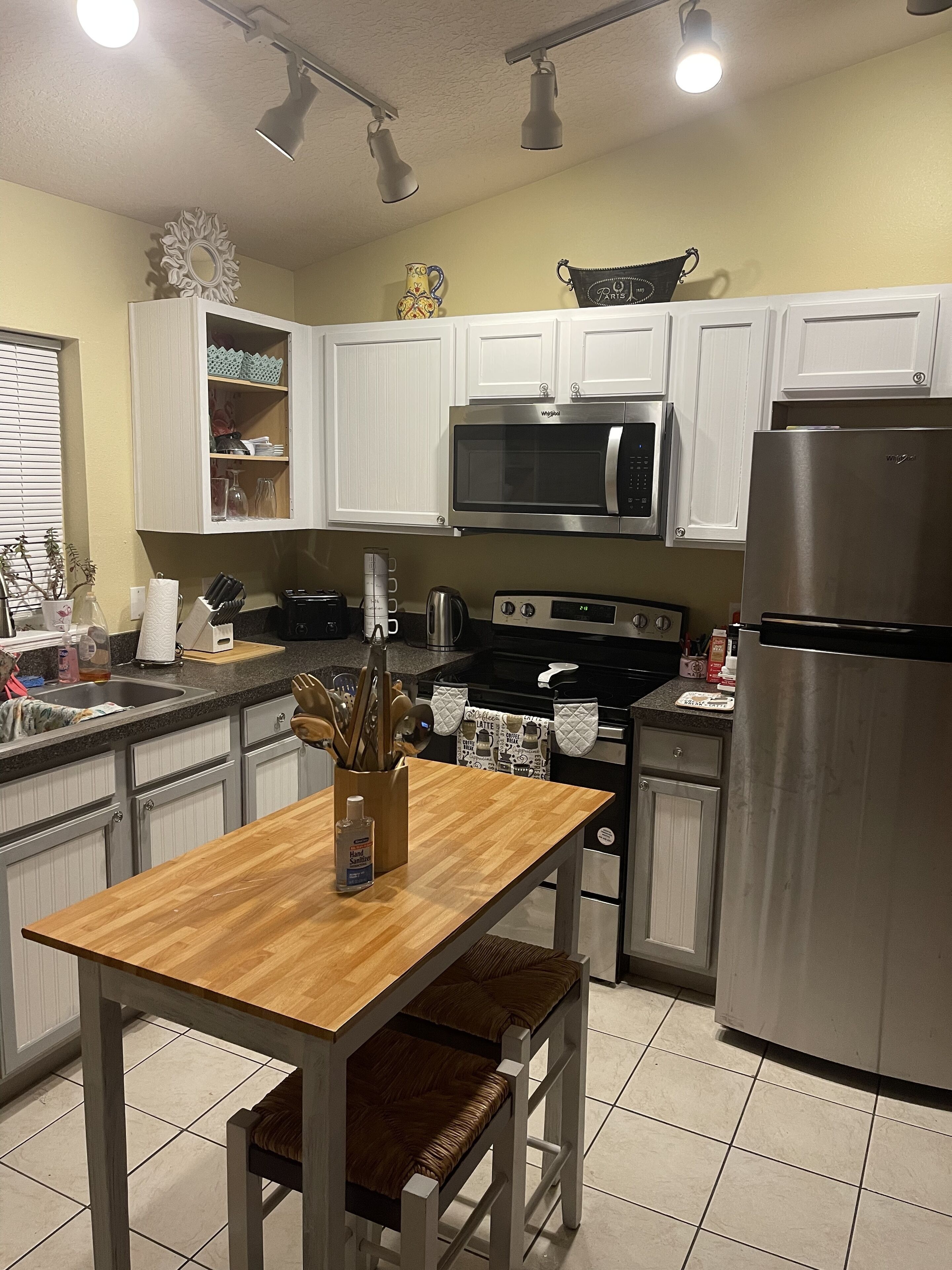 A modern kitchen with white cabinets, stainless steel appliances, and a wooden dining table.
