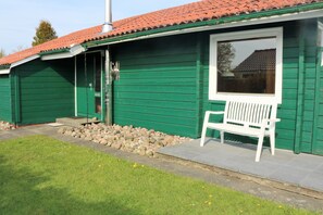 A green building with a tiled roof, a bench outside, and a window reflecting a house. - House Strandgut Damp (Damp)