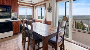 A kitchen with wooden cabinets, a dining table, and chairs. There is a view of a balcony with a railing and a scenic landscape. - ML148 Corner unit w/ views & fireplace connects to ML150 (rented separately) (Snowshoe)