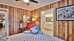 A bedroom with wooden paneling, a bed with a patterned bedspread, a red chair, a bedside table with a lamp, and a framed picture on the wall. - The Surf Shak-Vintage Coastal Charm (Murrells Inlet)
