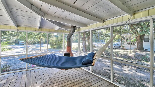 A hammock suspended from a ceiling in a covered outdoor area with a view of a residential street and greenery. - The Surf Shak-Vintage Coastal Charm (Murrells Inlet)