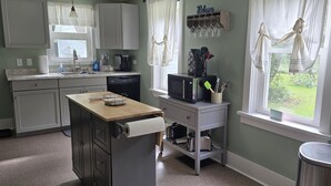 Una cocina con encimera de madera, lavavajillas, cafetera y ventana con cortinas.