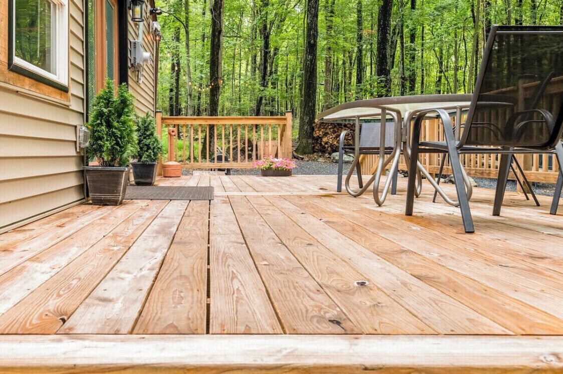 Una terraza de madera con una mesa y sillas, rodeada de un bosque.
