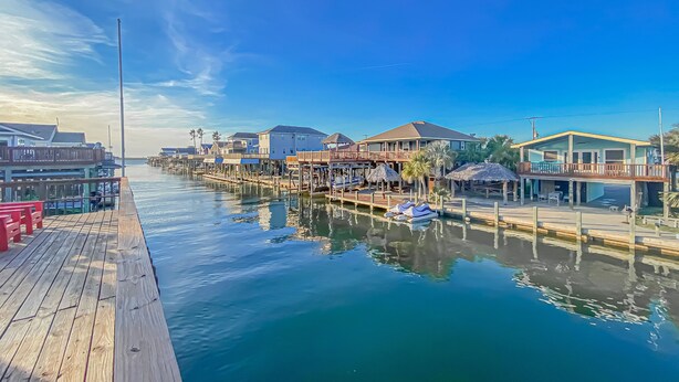 A waterfront property with a wooden dock, a boat, and houses with thatched roofs. - Island Tyme- Canal Waterfront Paradise with Sunset View! (Freeport)