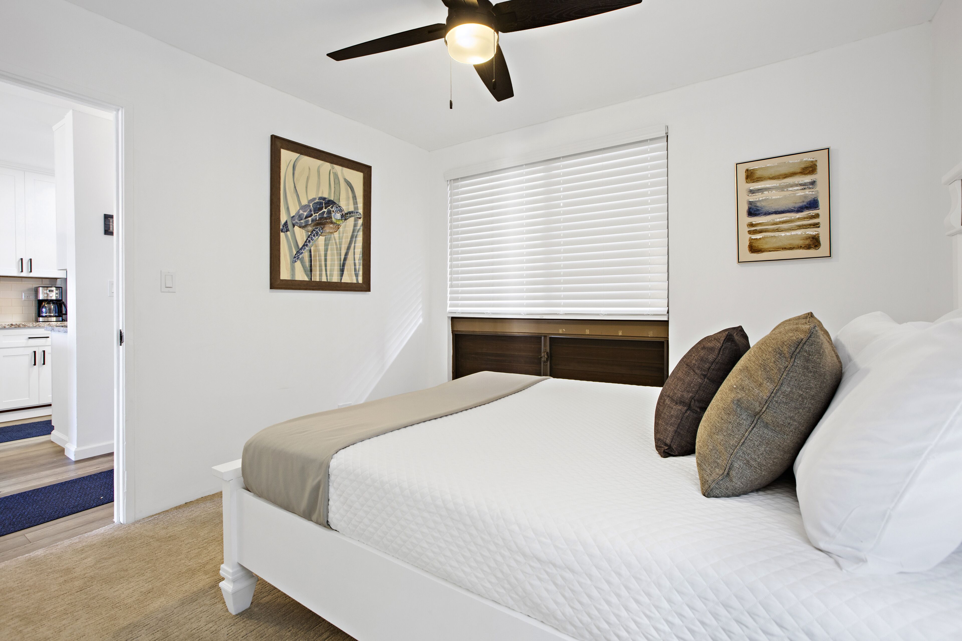 A bedroom with a bed, ceiling fan, artwork, and a window with blinds.