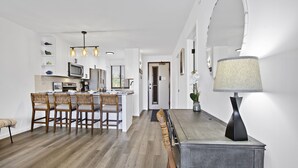 Et moderne køkken med hvide skabe, en mikrobølgeovn og et spiseområde med et træbord og stole.