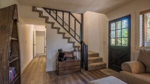 A staircase with a wooden finish and black railings, a wooden chest of drawers, a sofa, and a door with a window. - Modern Cabin w/ EV Car Charger and Pool Access (Dorrington)