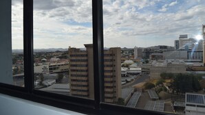 Blick auf eine Stadtansicht durch ein Fenster, mit hohen Gebäuden, blauem Himmel und Solaranlagen auf den Dächern.