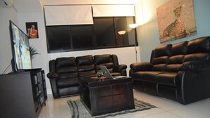 Una sala de estar moderna con dos sofás de cuero, una mesa de centro con una computadora portátil, un televisor y un cuadro en la pared.