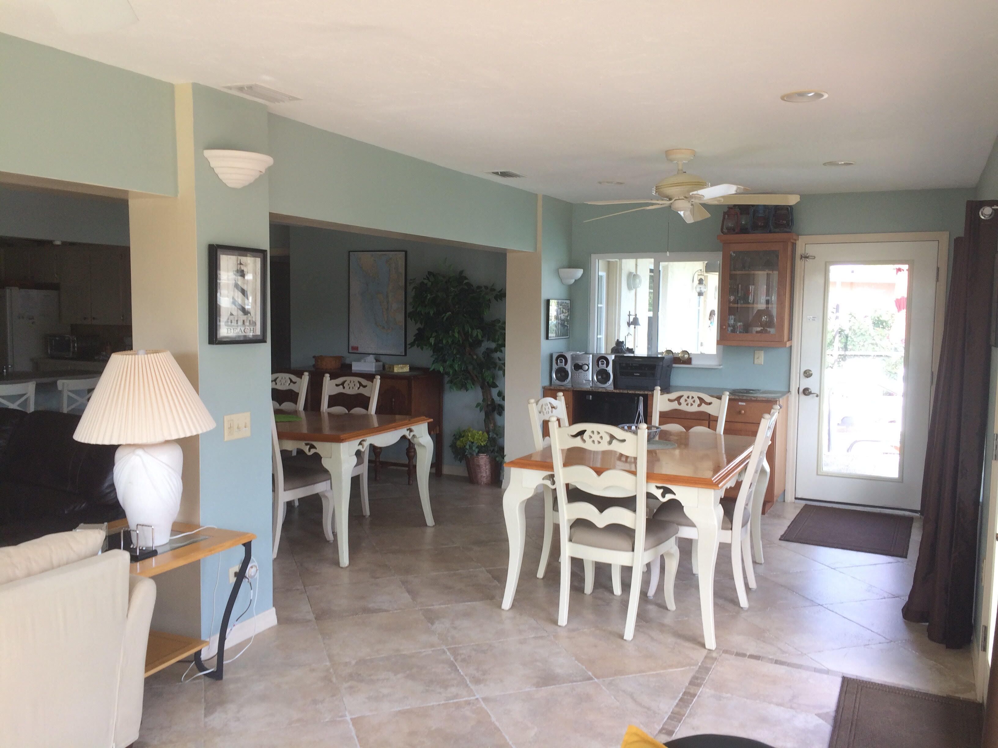 A dining area with a wooden table and white chairs, a lamp, and a potted plant.