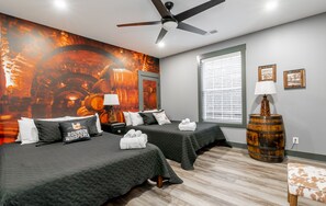 A hotel room with two beds, a large mural of barrels, a wooden barrel lamp, and a window with blinds.