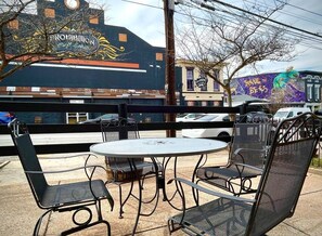 Outdoor seating with metal chairs and a round table, a building with a mural, and a street view.