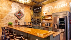 A bar area with a wooden bar counter, stools, a stainless steel refrigerator, and a brick wall with a 'High Ball' sign.