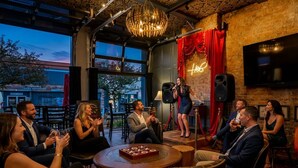 A group of people in a cozy, well-lit room with a stage, large windows, and a brick wall.