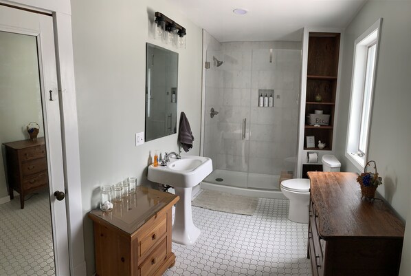 Un baño moderno con lavamanos blanco, tocador de madera, cabina de ducha con mampara de vidrio y un inodoro.