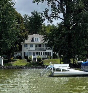 Una casa de dos pisos con un balcón, ubicada junto a un lago.