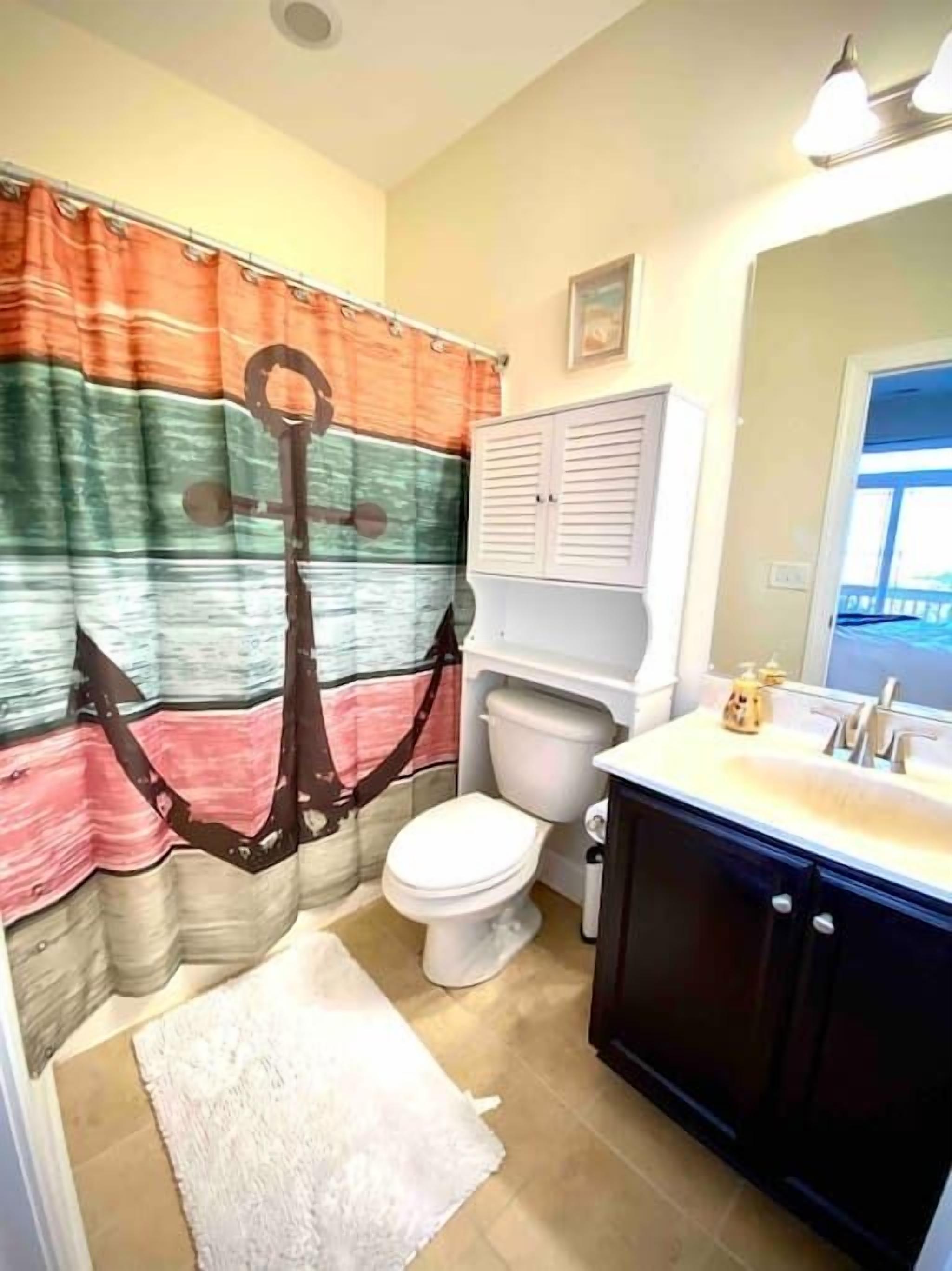 A bathroom with a striped curtain, a white toilet, a white sink with a mirror, and a white rug.