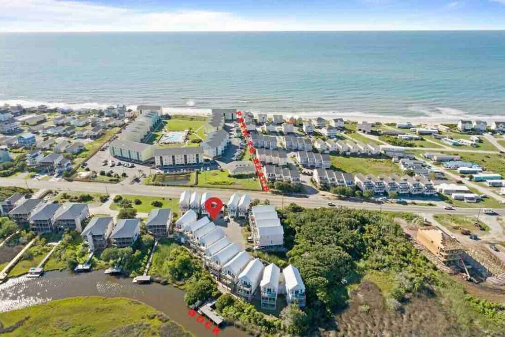 Vue aérienne d’un quartier résidentiel situé sur la côte, avec des maisons, une marina et un grand bâtiment doté d’un toit rouge distinctif.