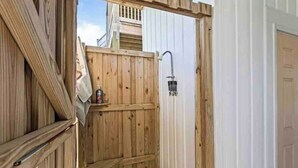A wooden outdoor shower area with a metal showerhead, a wooden bench, and a bottle on the bench. - Your family will be close to everything when you stay at this centrally-located beach oasis (Surf City)