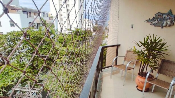 Een balkon met een hek van gaas, planten in potten en een bank.