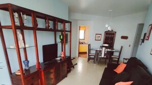 Een woonkamer met een zwarte bank, een houten tv-meubel en een eethoek met een tafel en stoelen.