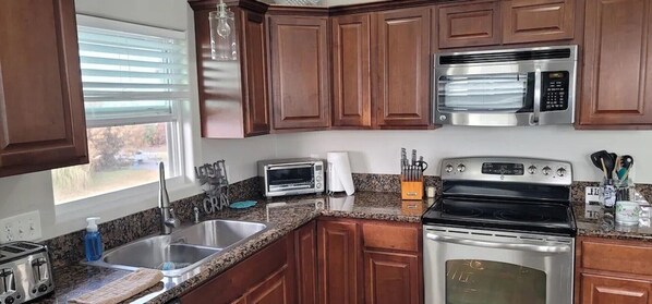 A kitchen with wooden cabinets, a stainless steel microwave, a toaster, and a sink.