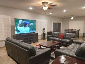 A living room with a flat-screen TV, leather sofas, a dining table, and a ceiling fan.