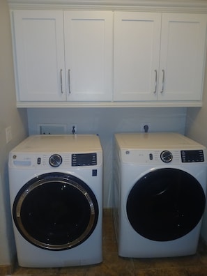 Two front-loading washing machines with control panels, a white wall, and a white door above them.