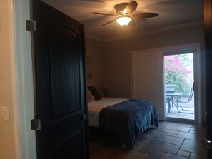 A bedroom with a bed, a ceiling fan, and a door leading to a patio with outdoor furniture.