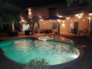 A swimming pool with a water feature, surrounded by outdoor seating and string lights.