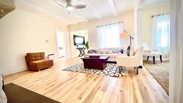 Un salon spacieux avec un canapé marron, un fauteuil blanc, une table basse en bois et un tapis à motifs.