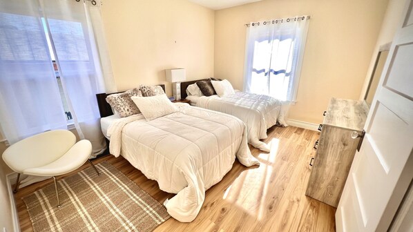 A bedroom with two beds, a chair, a bedside table, and a wooden wardrobe.