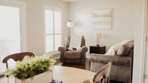 A living room with a sofa, armchair, and a dining table with a plant. - Serene on 17 Pointe Royale Walk-In Condo, Water Views (Branson)