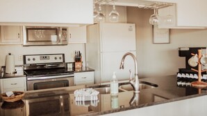 A modern kitchen with stainless steel appliances, a central island with a sink, and hanging light fixtures. - Serene on 17 Pointe Royale Walk-In Condo, Water Views (Branson)
