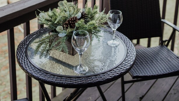 A round glass table with two wine glasses and a centerpiece on a wooden deck. - Serene on 17 Pointe Royale Walk-In Condo, Water Views (Branson)