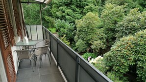 Ein Balkon mit Glastisch und Korbstühlen, umgeben von üppiger Bepflanzung und verschiedenen Pflanzen.