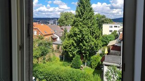 Blick aus einem Fenster auf ein Wohngebiet mit einem großen Baum, Häusern und einem klaren Himmel.