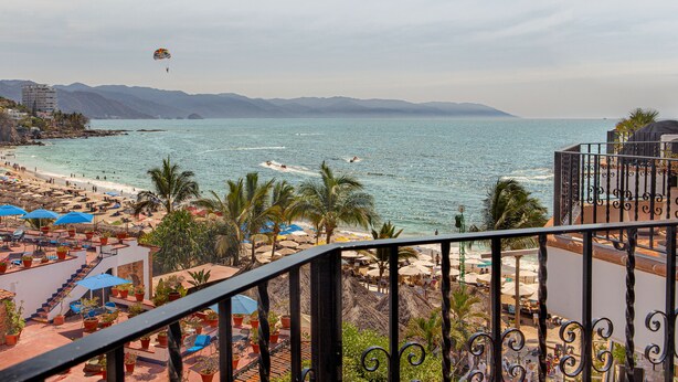 A beach resort with a view of the sea, palm trees, and a parasail in the distance. - La Palapa beachfront fully renovated condo!  In the heart of the Romantic Zone. (Puerto Vallarta)