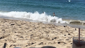 A beach view with a table and drinks, waves crashing onto the shore, and a distant boat. - La Palapa beachfront fully renovated condo!  In the heart of the Romantic Zone. (Puerto Vallarta)