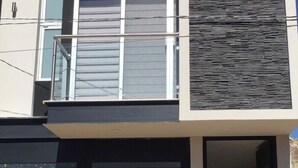 A modern two-story house with a garage door, a balcony, and a textured wall. - La cuna del buen vestir (Colonia la Cruz)