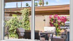 An outdoor patio with a grill, seating, and a view of a garden with flowers and palm trees. - Desert Retreat Relax, Recharge, Views, Resort Living, Office + Monthly Discount (Palm Springs)